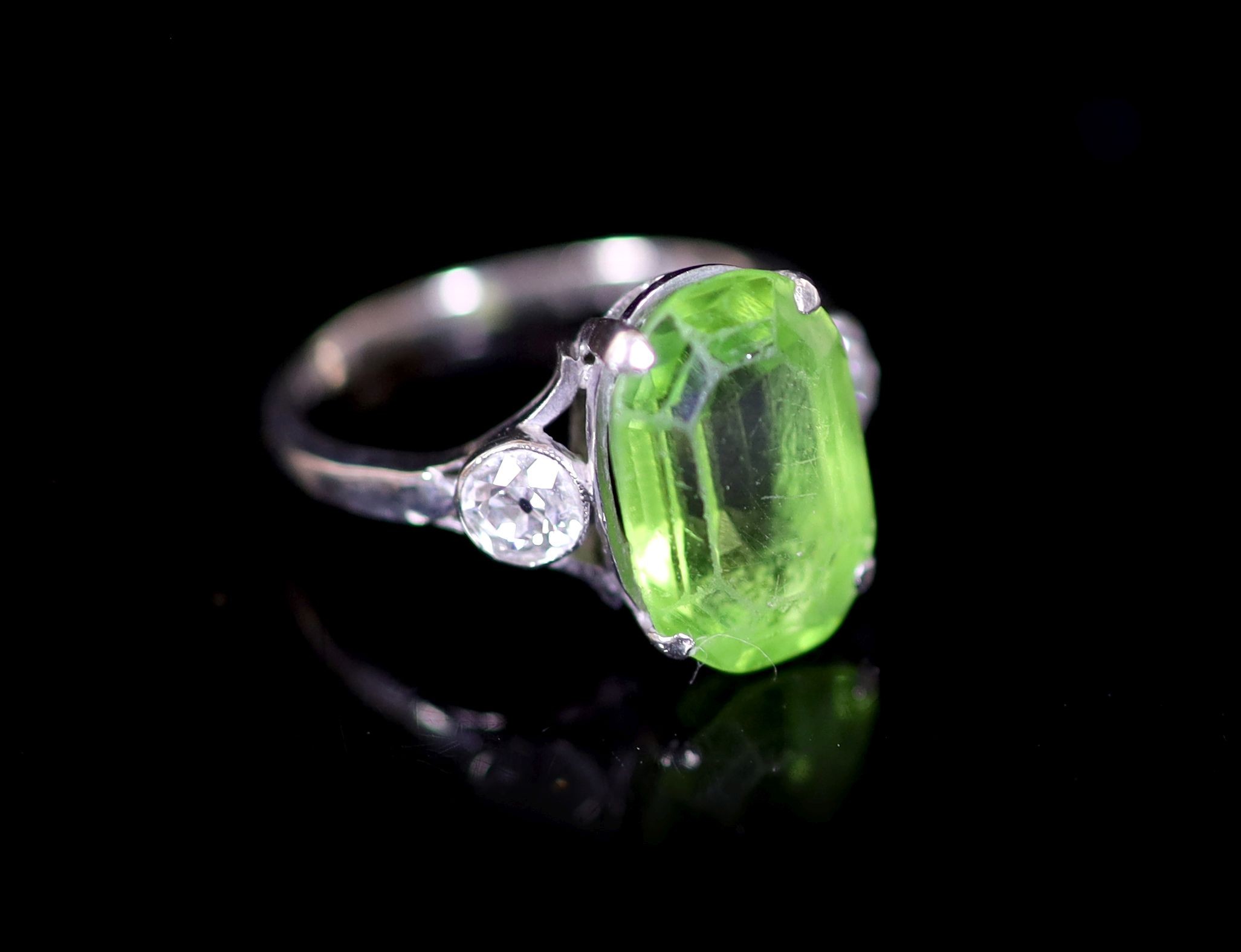 A 9ct white gold oval cut peridot set dress ring, with diamond set shoulders